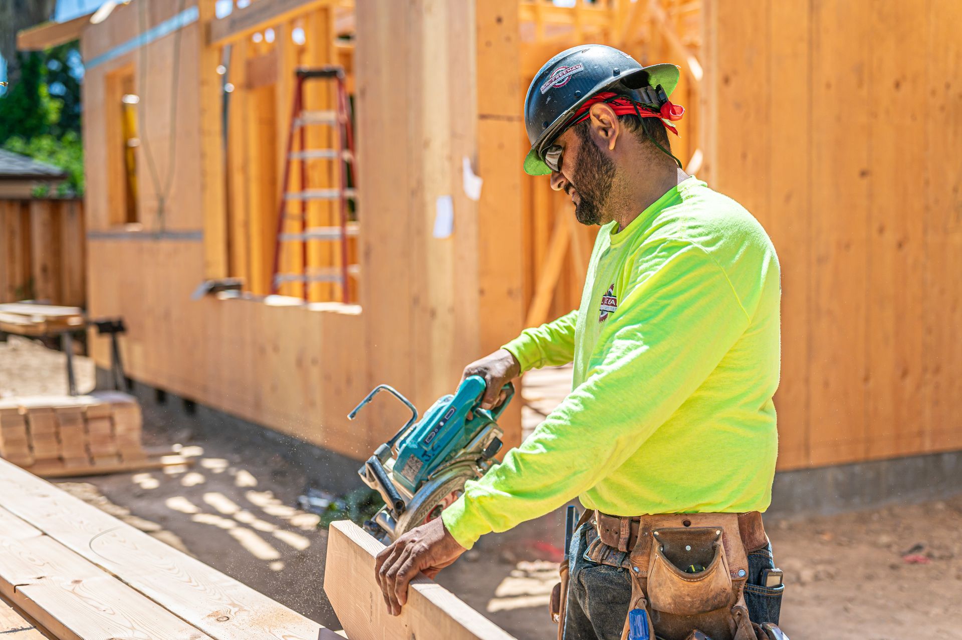 Construction worker in neon shirt using a circular saw on lumber beside a wooden building