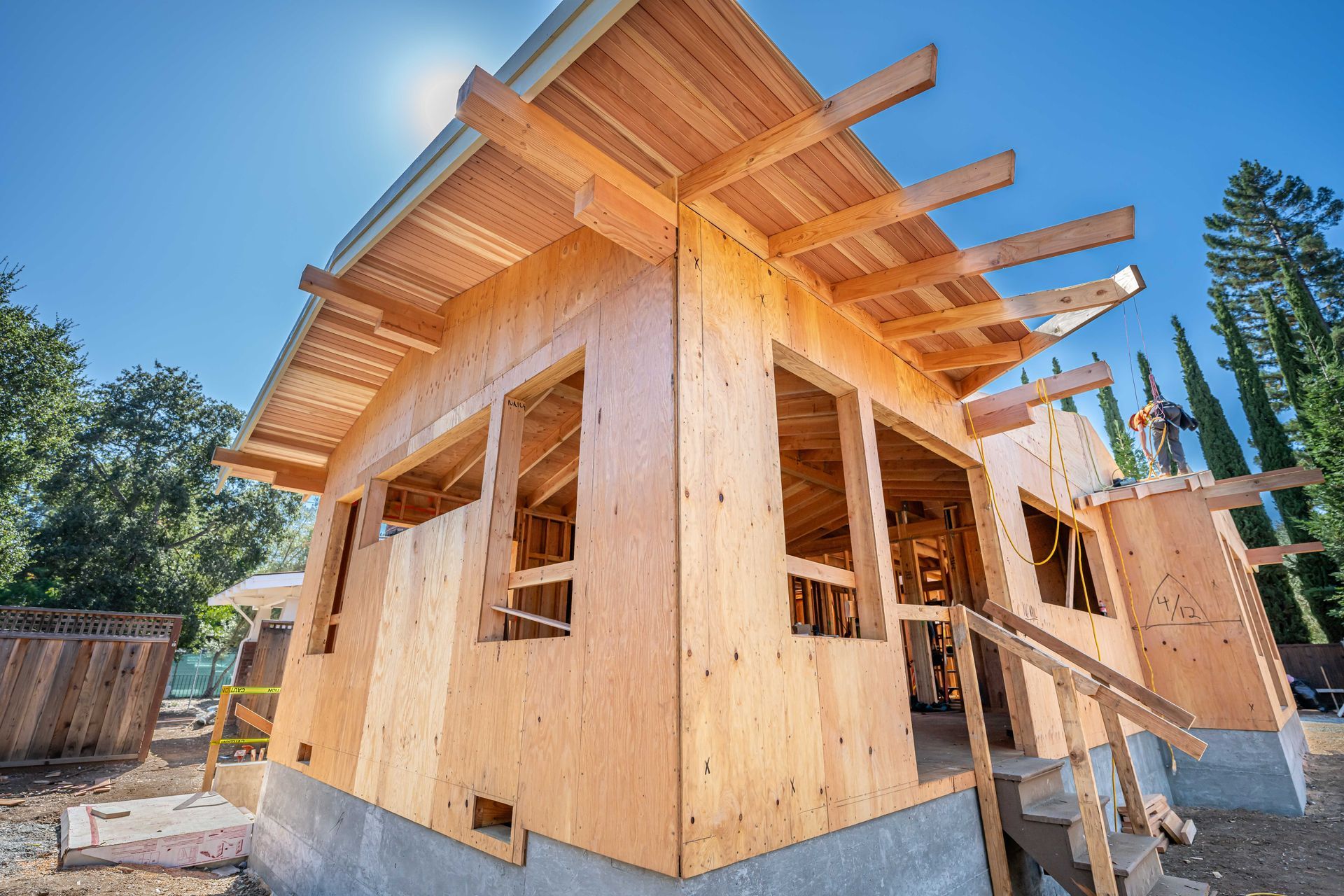 Partially built wooden house with exposed framing and roof beams on a sunny construction site