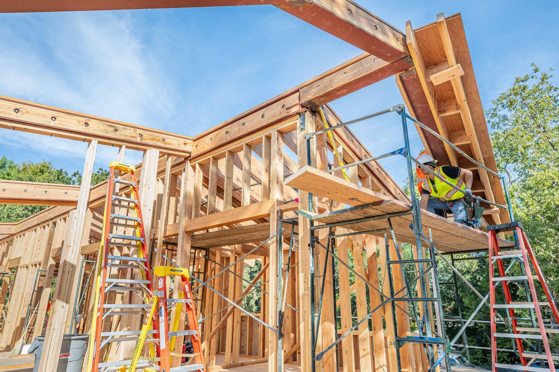 House framing under construction with workers on ladders and scaffolding on a sunny day