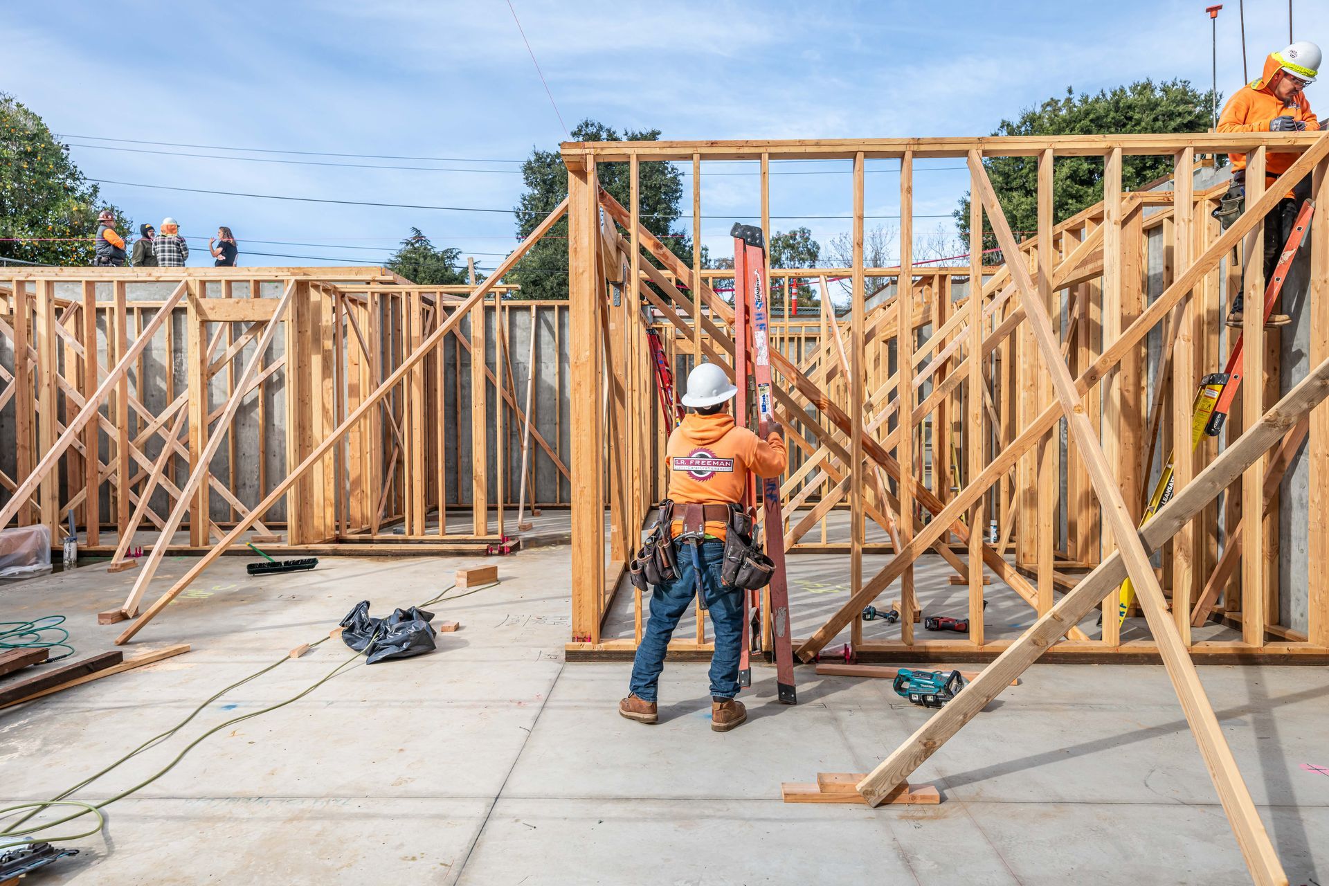 Construction workers framing walls at a building site with wooden beams and concrete slab