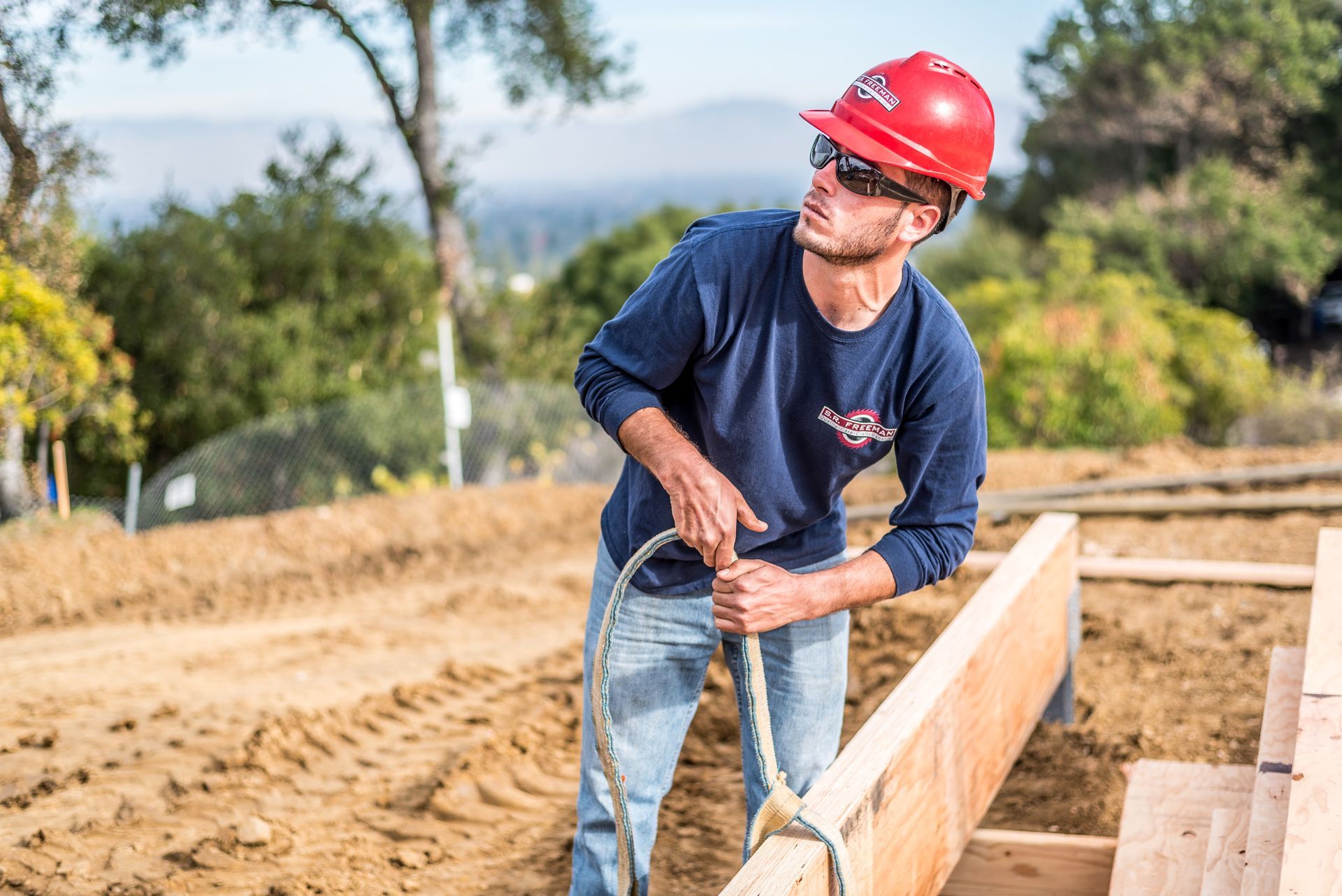 Construction worker in red hard hat measuring lumber at a building site