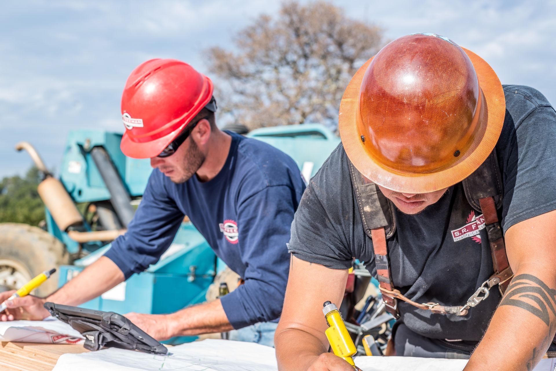 Two workers in hard hats leaning over plans at a construction site outdoors