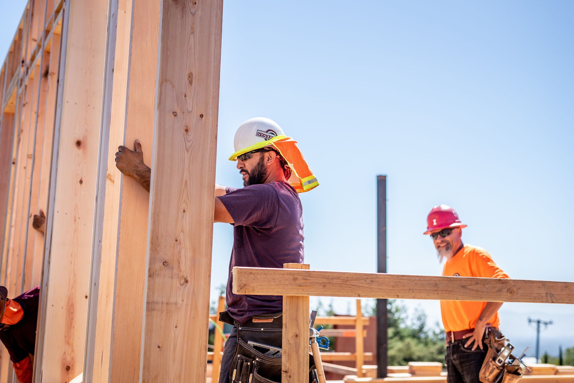 Construction workers framing a wooden wall at a building site under a clear blue sky