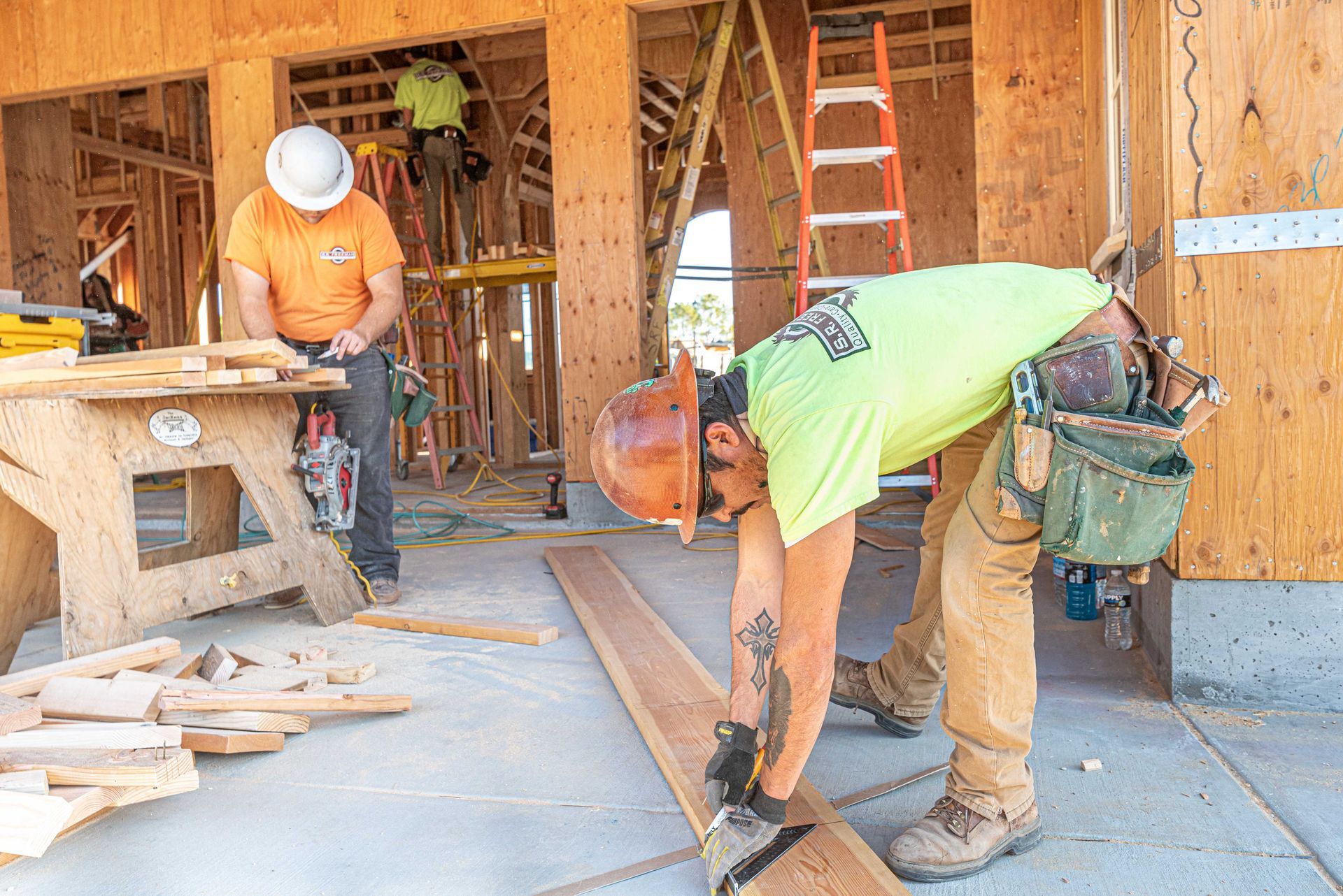 Two construction workers in a wood-framed building measuring and cutting flooring boards