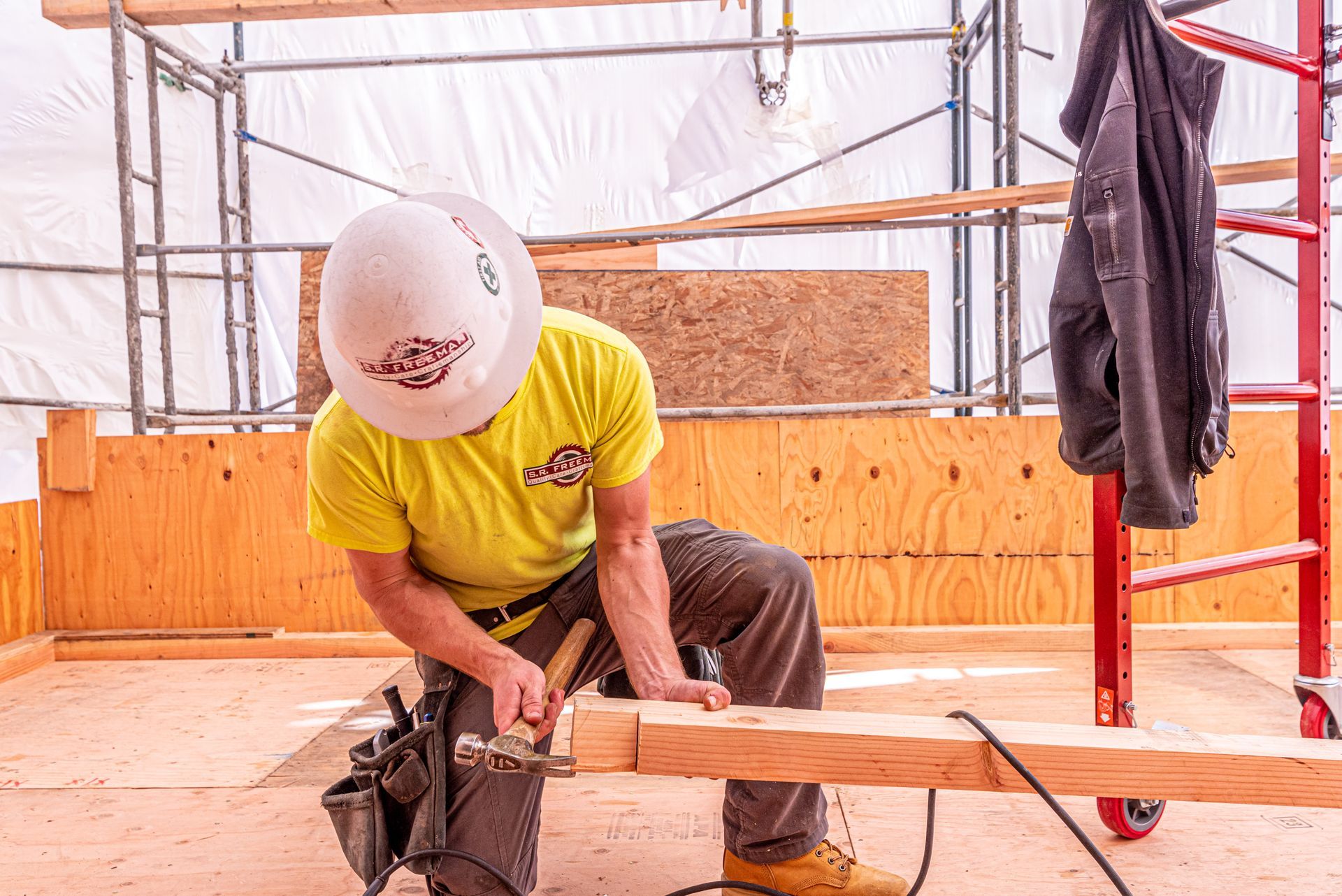 Worker in a yellow shirt sawing a wooden beam at a construction site
