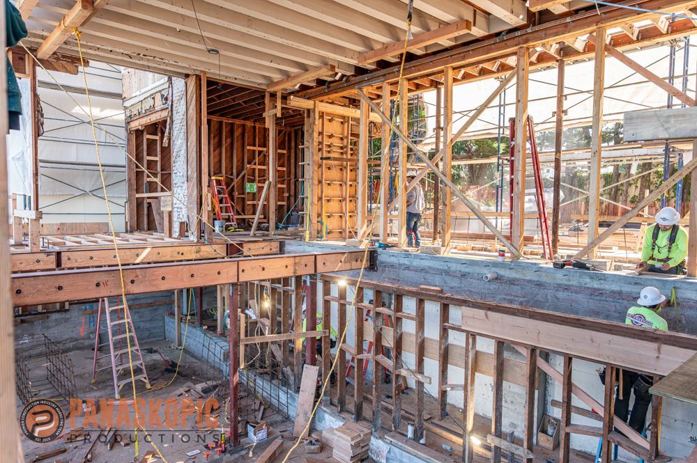 Construction site interior with exposed wooden framing, open floor, and a worker in a safety vest