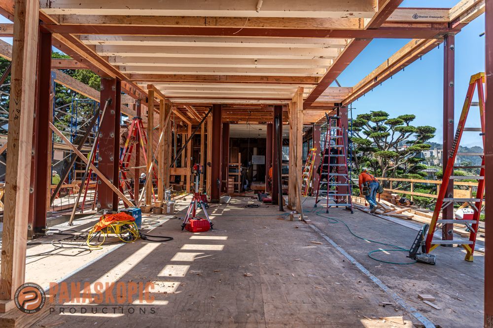 Wood-framed building under construction with ladders, tools, and sunlight streaming across the floor