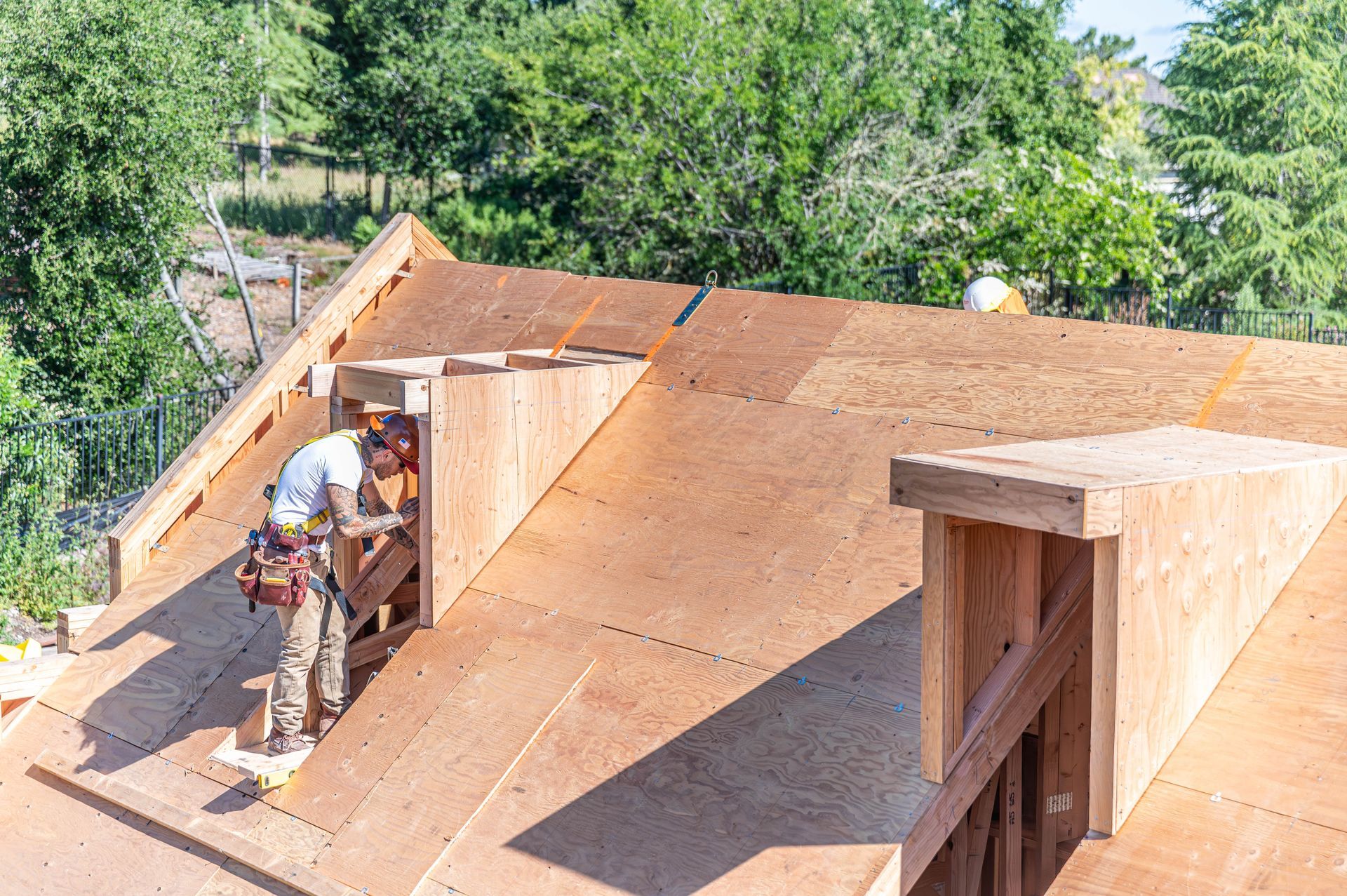 Workers installing plywood roofing on a house under construction, with trees in the background