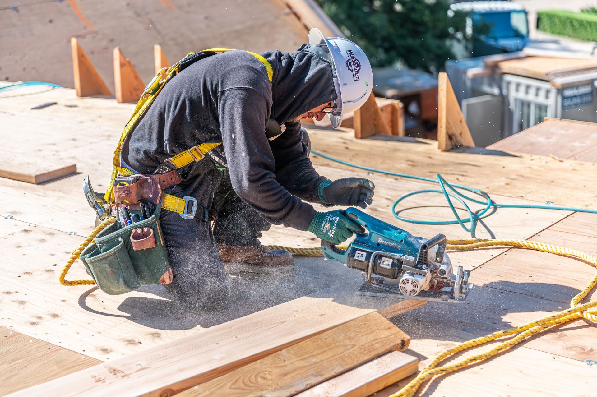 Construction worker cutting wood with a circular saw on a rooftop, sparks flying.