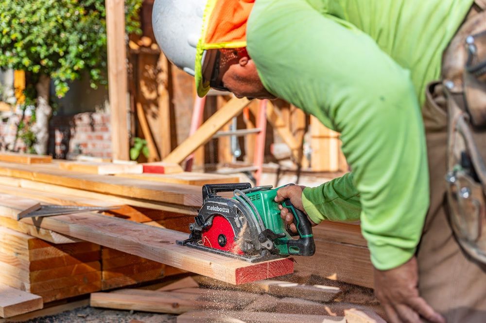 Worker in green shirt using a circular saw to cut wood at a construction site