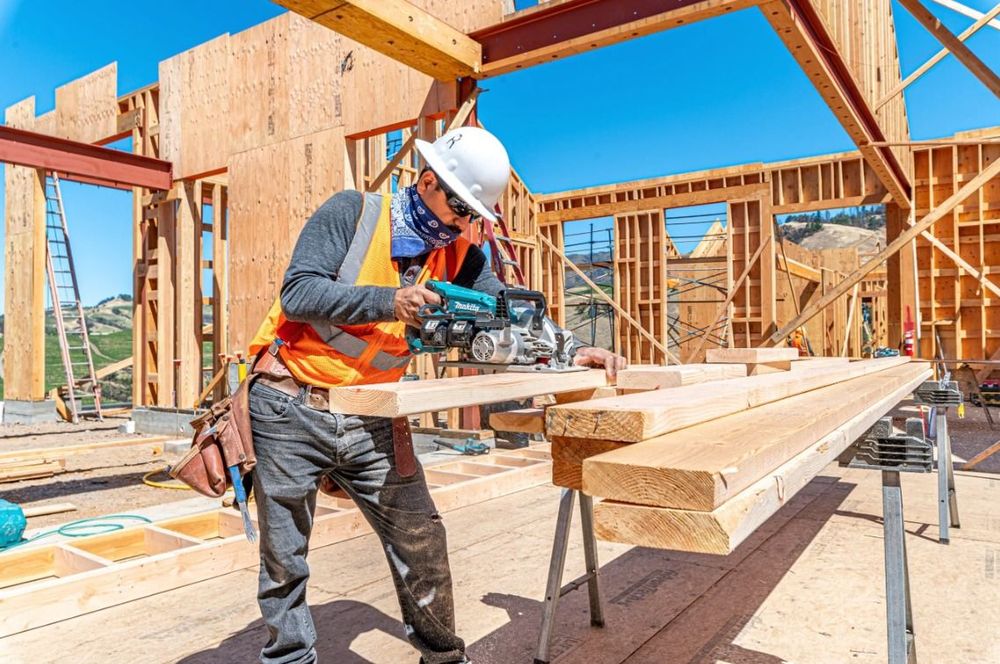Construction worker cutting lumber on a house frame with a circular saw.
