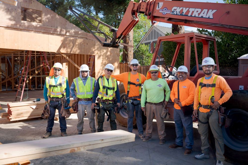 Construction crew in hard hats standing beside an orange SkyTrak forklift at a worksite