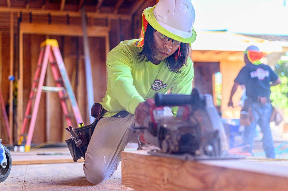Worker in a hard hat cutting wood with a circular saw at a construction site