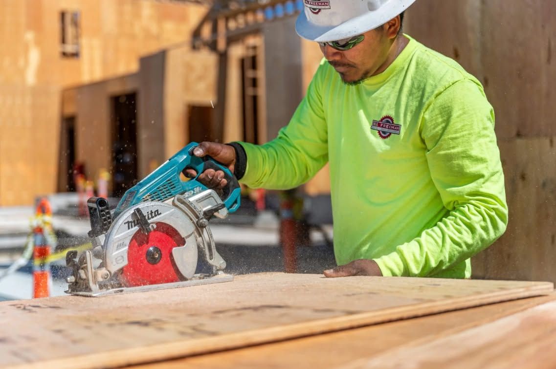 Construction worker cutting wood with a circular saw, wearing a neon green shirt and white hard hat