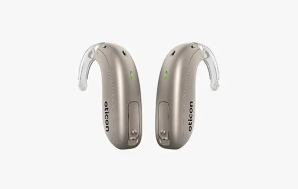 Par de audífonos retroauriculares de color beige con luces indicadoras verdes sobre fondo blanco.