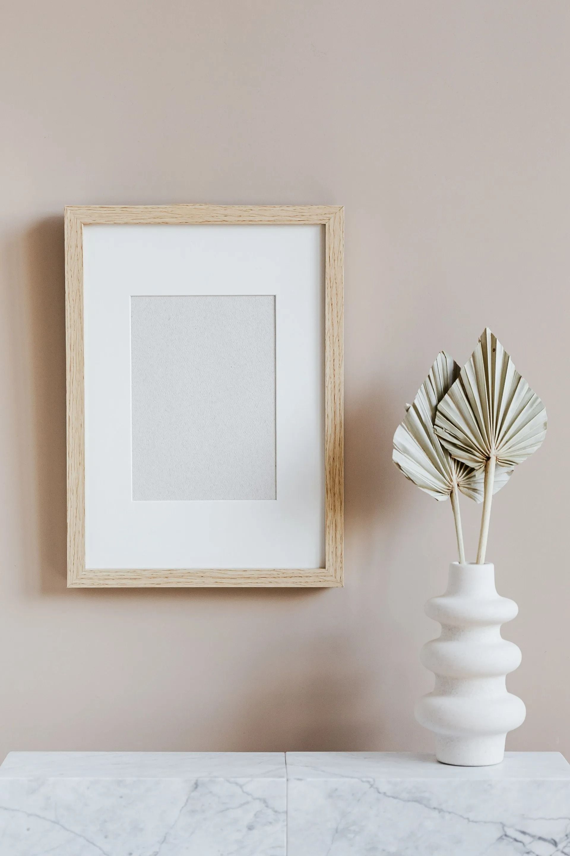 Minimalist wall decor with framed art and a white vase of dried leaves on a marble surface
