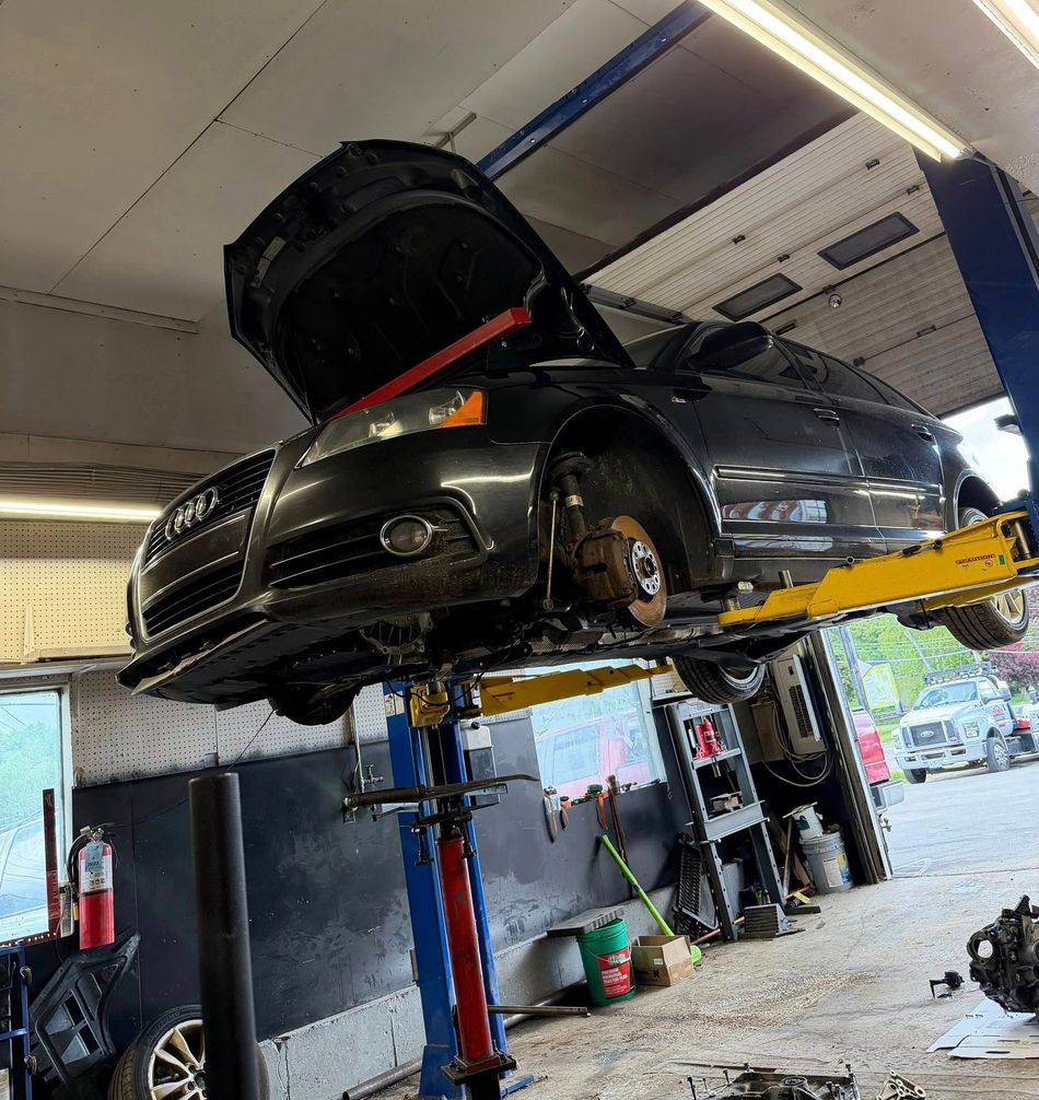 Black car on a lift in an auto shop, hood open and front wheel removed during repair.