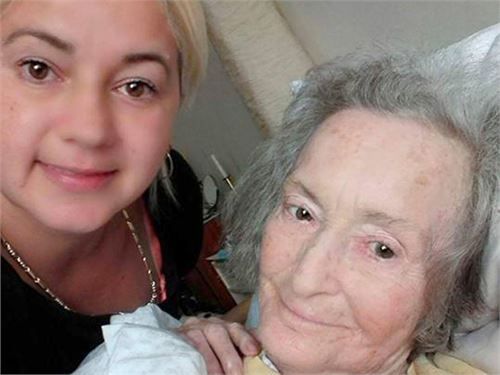 Eine Frau macht ein Selfie mit einer älteren Frau im Bett. Beide lächeln.