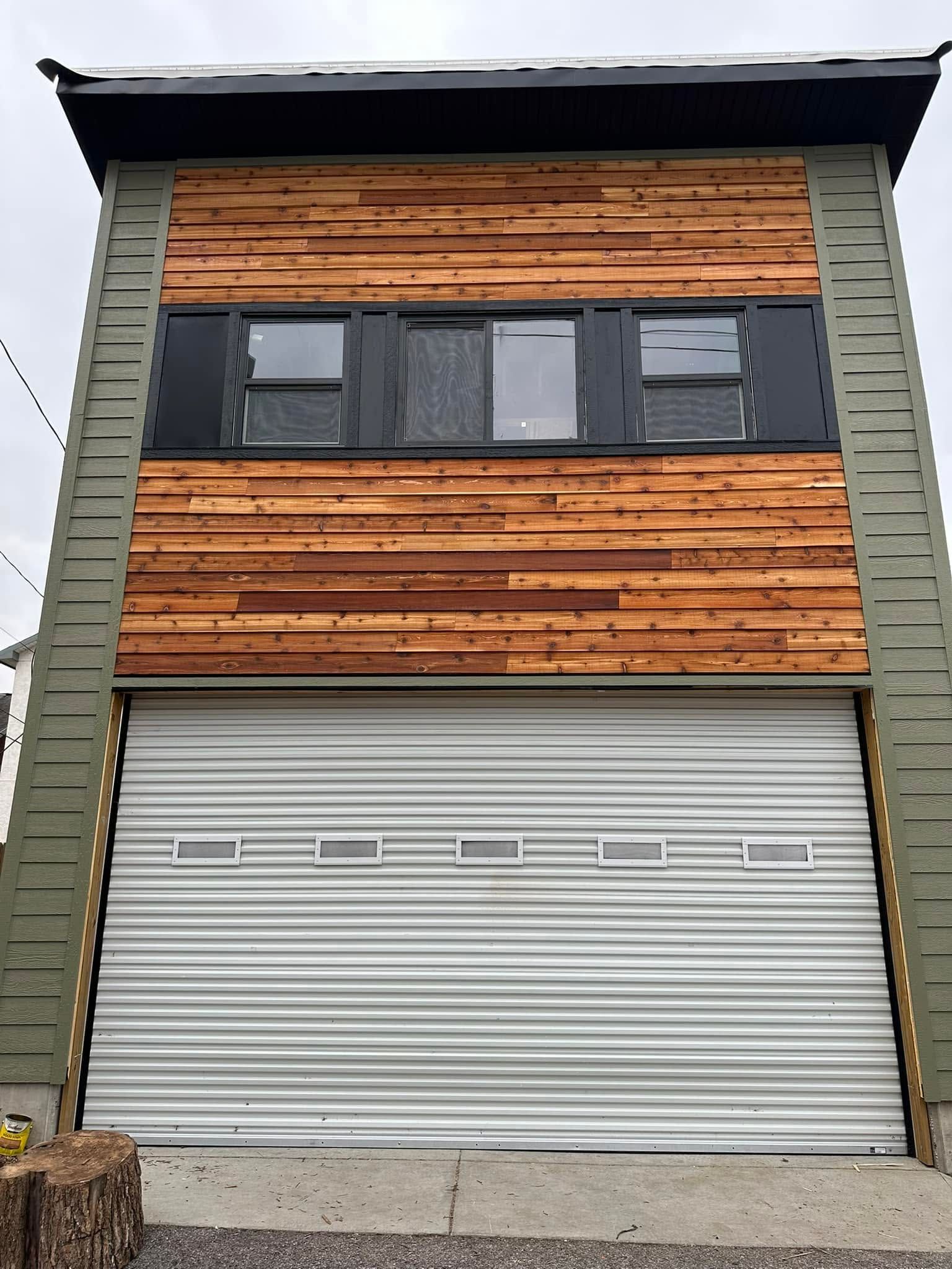Wood-fronted two-story building facade with black windows and a large gray roll-up garage door Wood-fronted two-story building facade with black windows and a large gray roll-up garage door