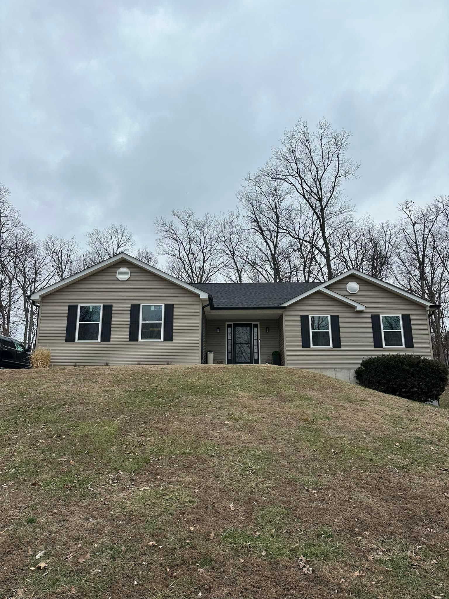 Single-story beige house with green shutters on a grassy hill under a cloudy sky Single-story beige house with green shutters on a grassy hill under a cloudy sky