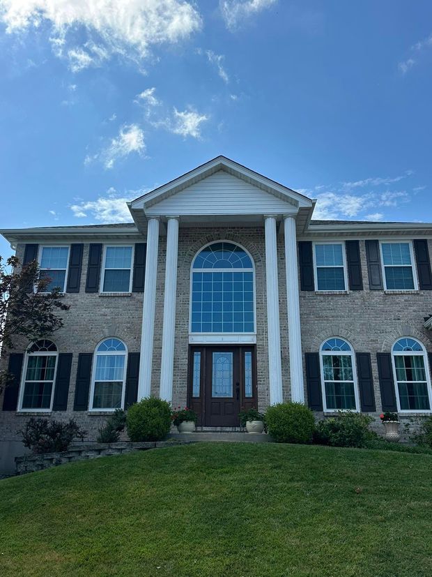 Two-story brick house with white columns, arched windows, and a manicured lawn under a blue sky