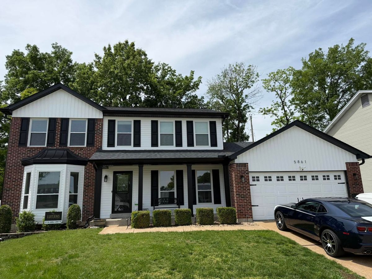 Suburban two-story house with black shutters, brick accents, and a black car parked in the driveway