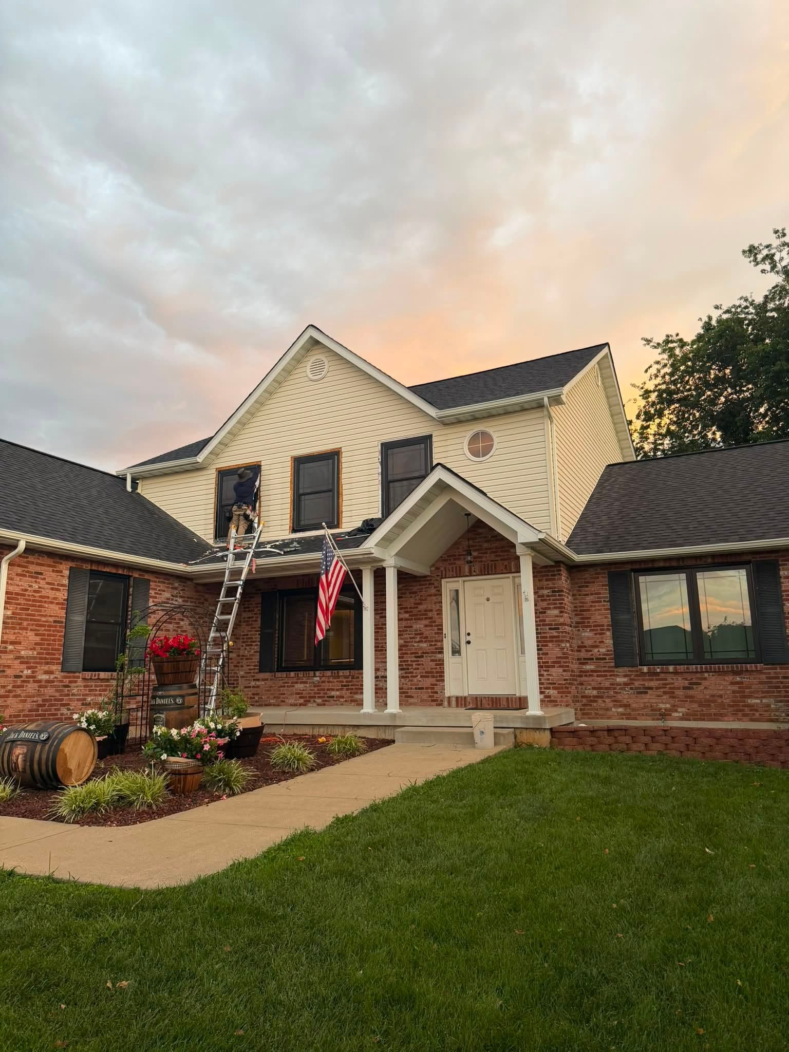 Front view of a cream-colored house with an American flag, brick accents, and a neatly kept lawn at sunset Front view of a cream-colored house with an American flag, brick accents, and a neatly kept lawn at sunset