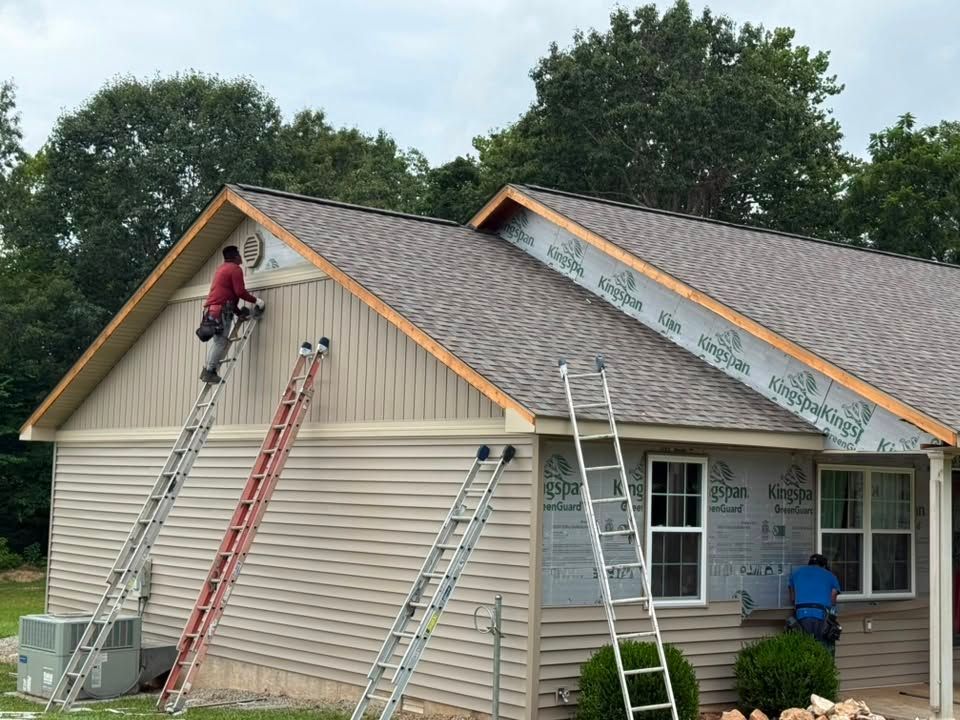 Workers on ladders repairing a house roof with new shingles and siding Workers on ladders repairing a house roof with new shingles and siding