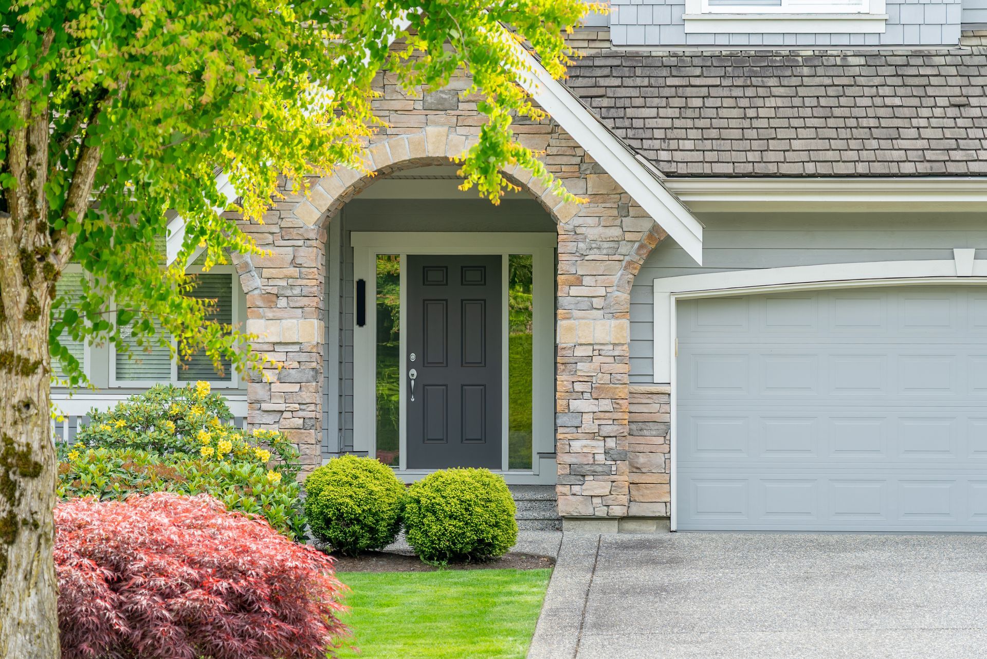 Suburban house entrance with stone facade, dark front door, garage, and landscaped front yard Suburban house entrance with stone facade, dark front door, garage, and landscaped front yard