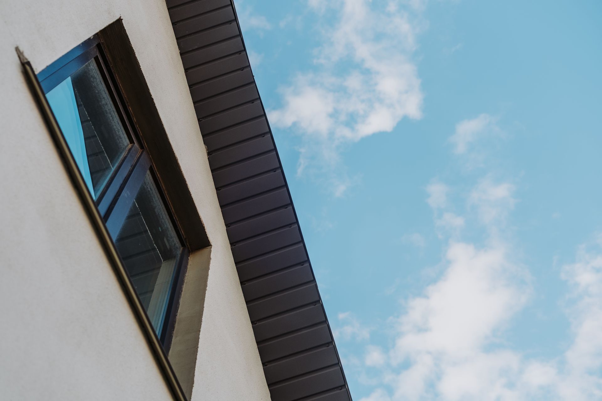 Angled view of a white building with a dark window frame against a blue sky with clouds Angled view of a white building with a dark window frame against a blue sky with clouds