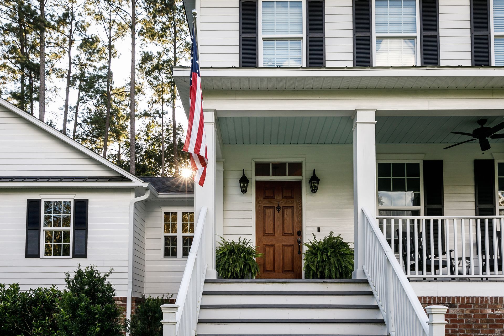 Front porch of a white house with an American flag and wooden front door Front porch of a white house with an American flag and wooden front door