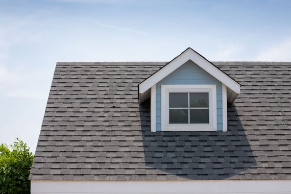 Gray shingled roof with a white dormer window under a blue sky