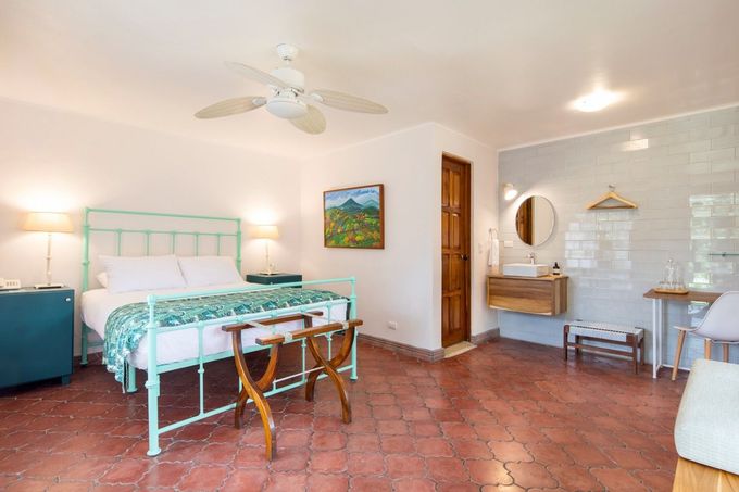 A bedroom with a king size bed , a ceiling fan , a sink and a painting on the wall.