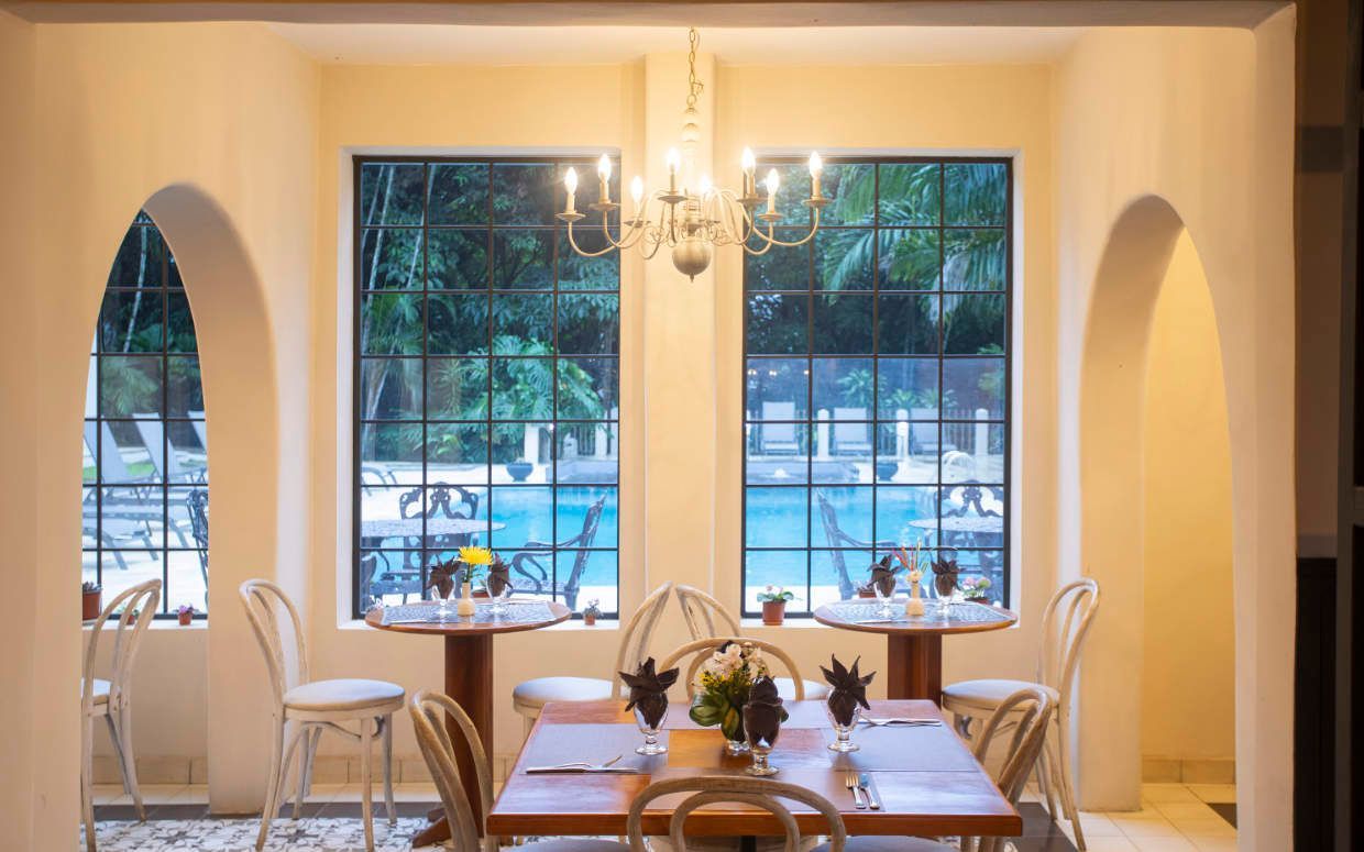 A dining room with tables and chairs and a pool in the background.