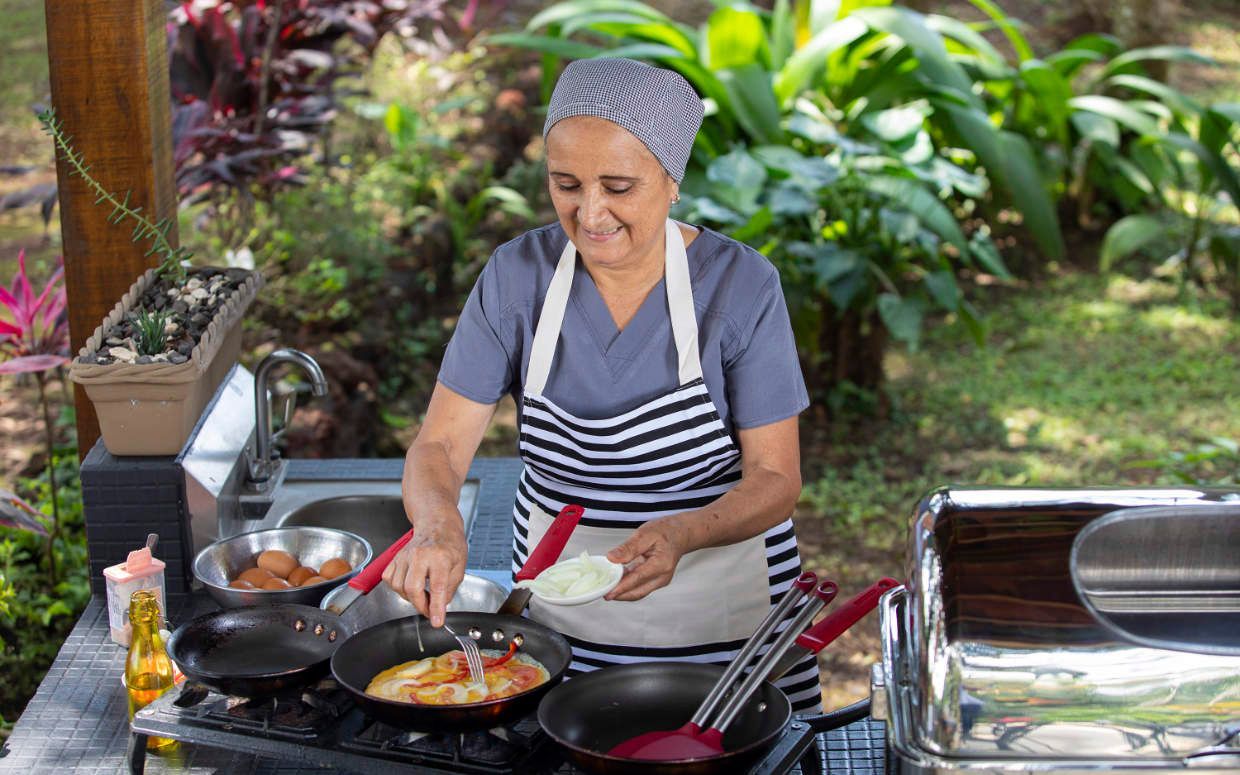 A woman is cooking food in a pan on a stove outside.
