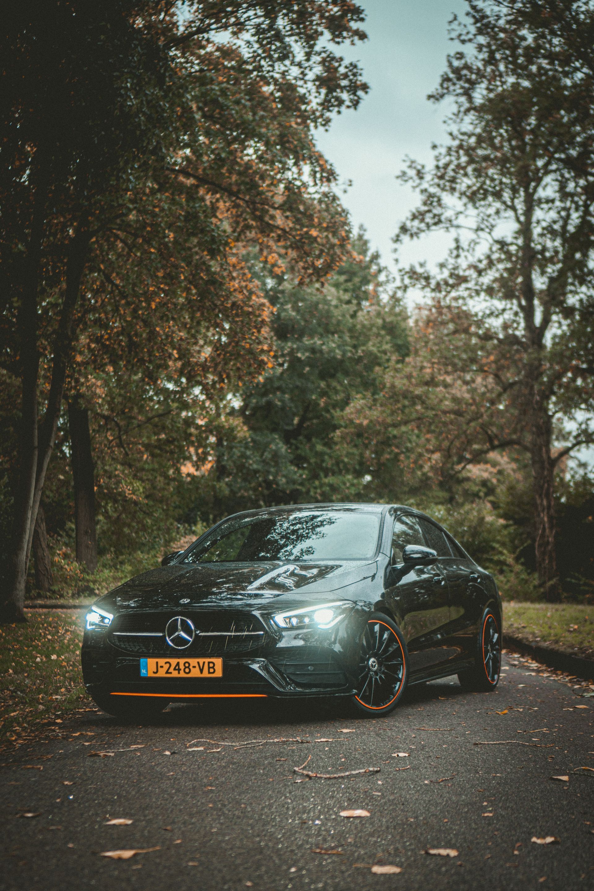 Een zwarte Mercedes-Benz sedan op een met bladeren bedekte weg, omringd door bomen.