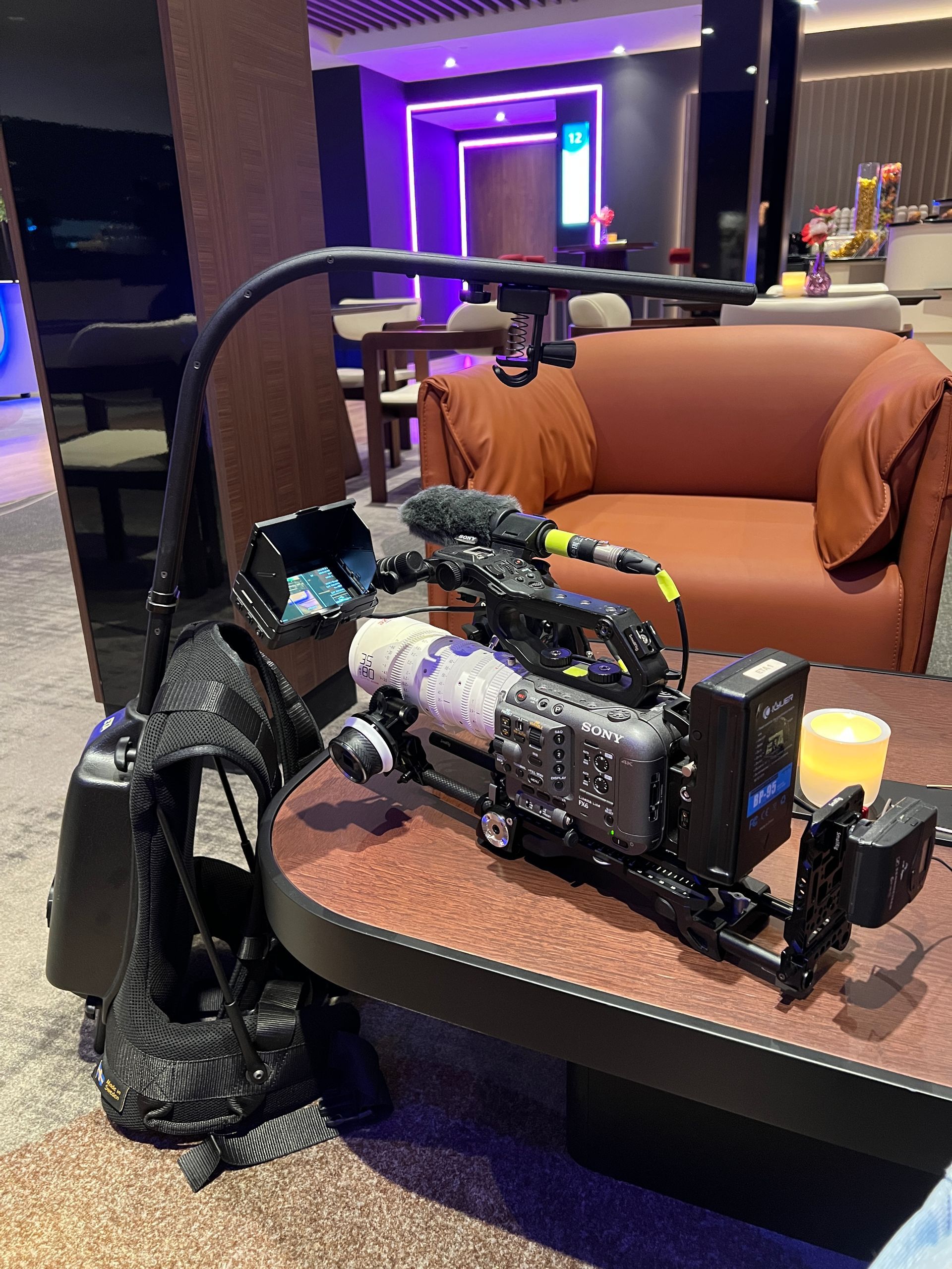 Een videocamera staat op een tafel, met een statief eraan bevestigd. Achtergrond: hotellobby.