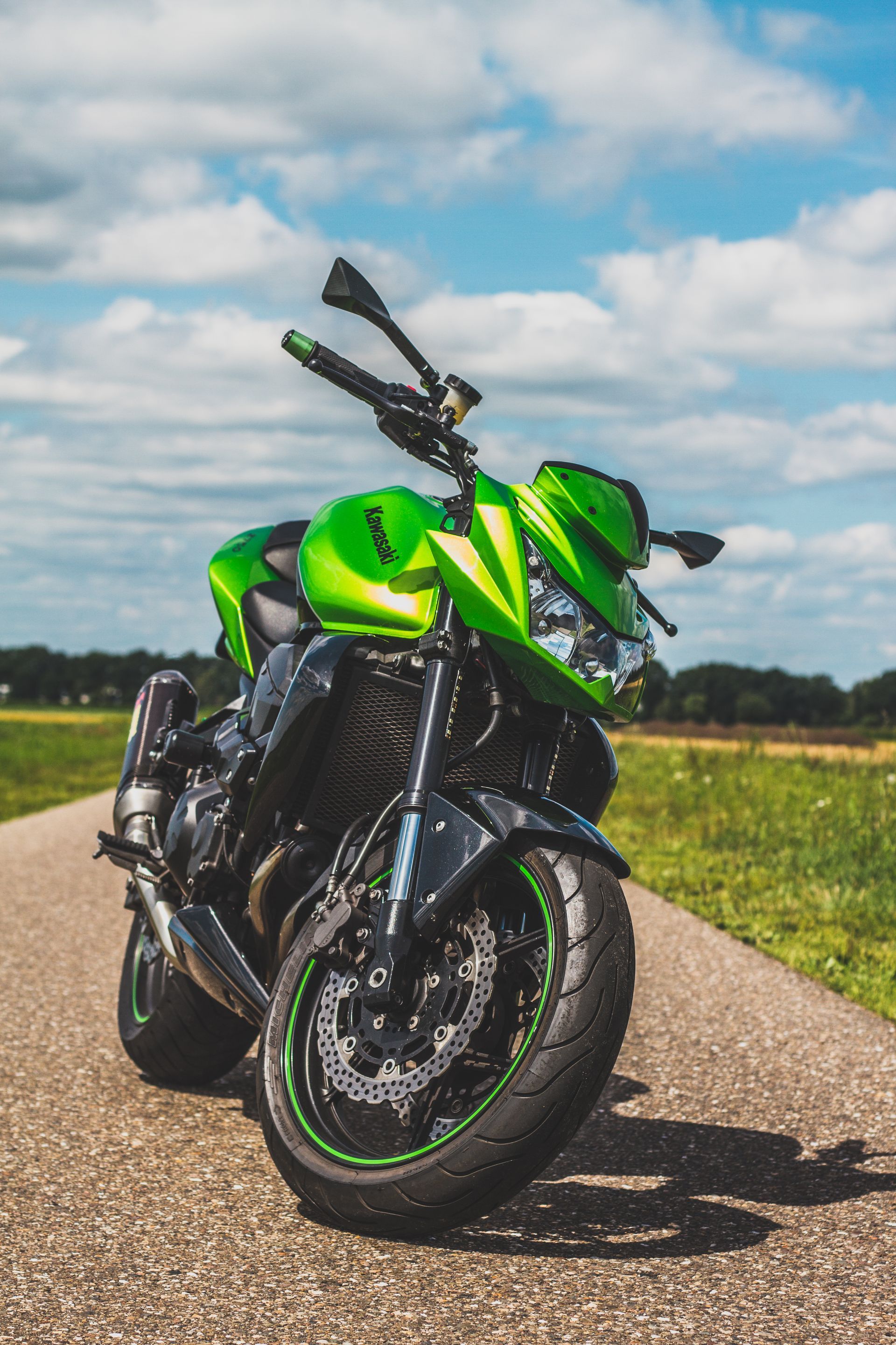 Een groene en zwarte Kawasaki-motorfiets staat geparkeerd op een geasfalteerde weg, met een helderblauwe lucht op de achtergrond.