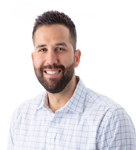 A man with a beard is wearing a plaid shirt and smiling.