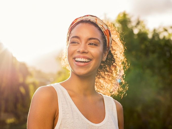 A woman wearing a headband and a white tank top is smiling.