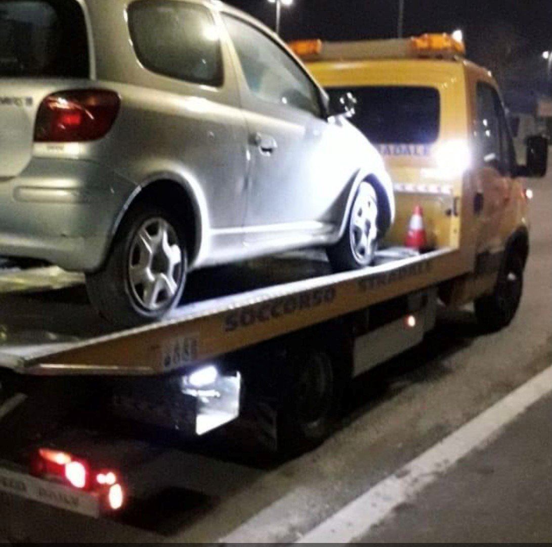 Un'auto argentata è seduta sopra un carro attrezzi giallo con la scritta
