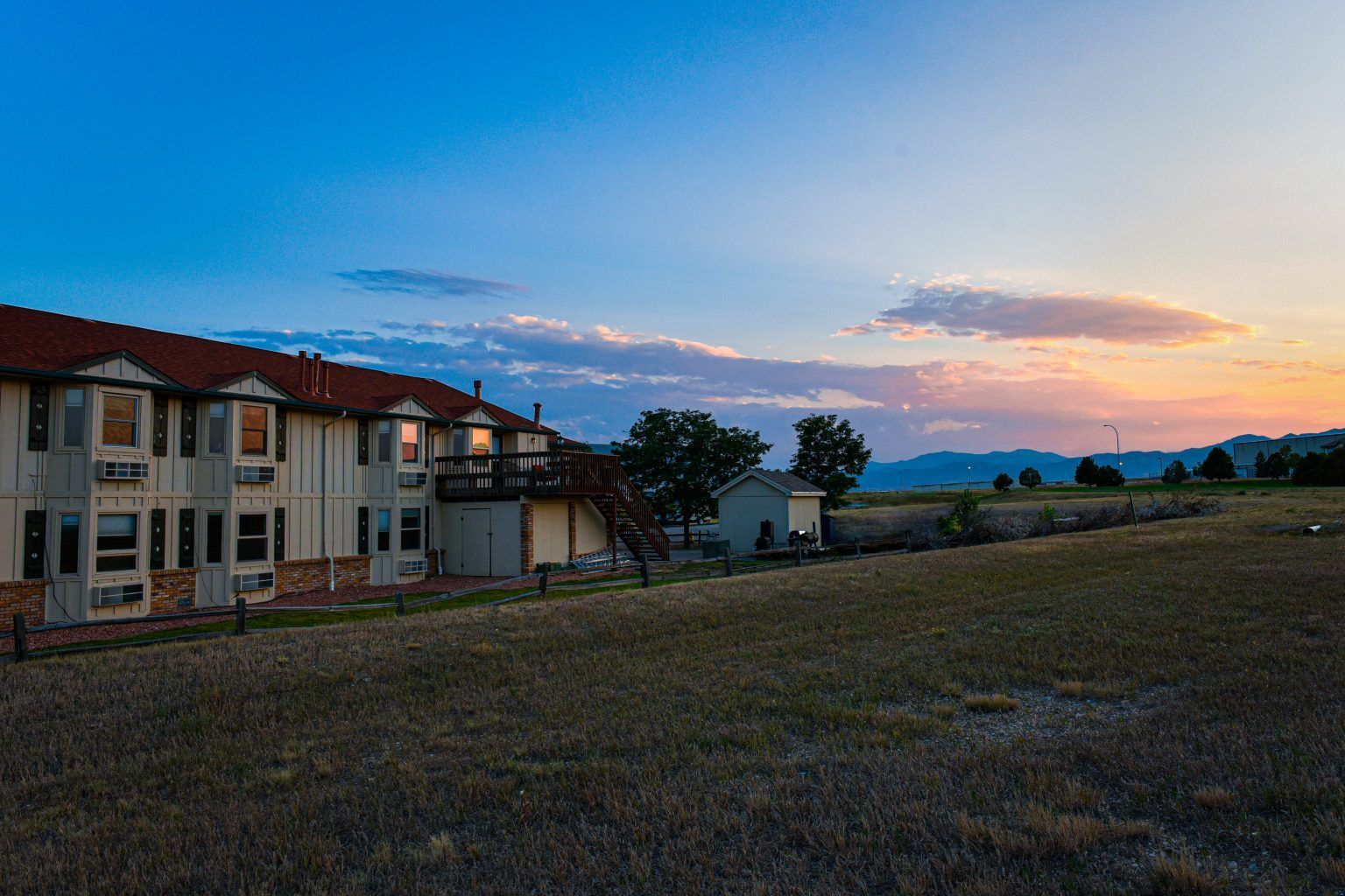 A large building with a red roof is sitting in the middle of a field at sunset.
