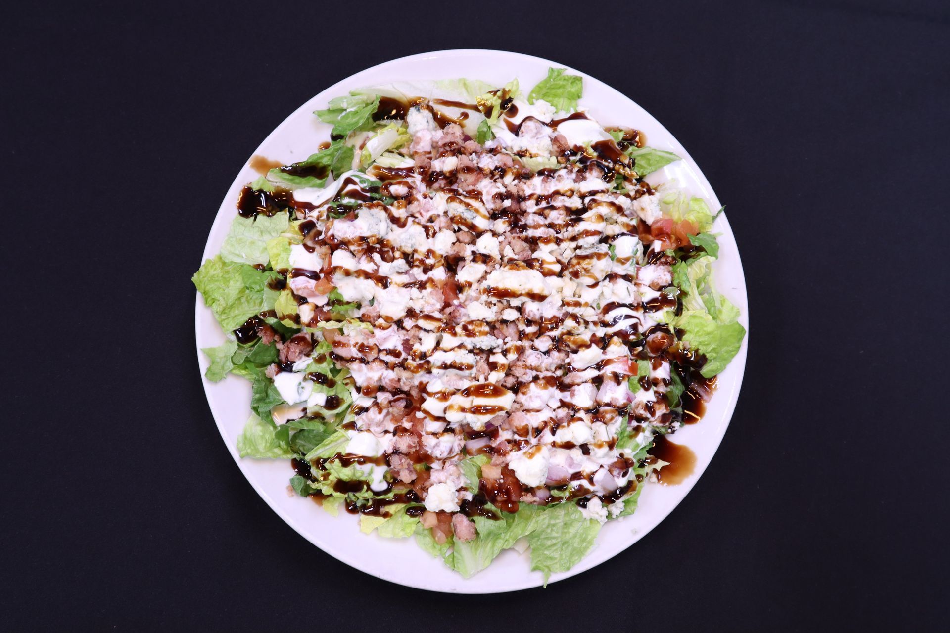 Salad with leafy greens, cheese, and balsamic glaze on a white plate, dark background.