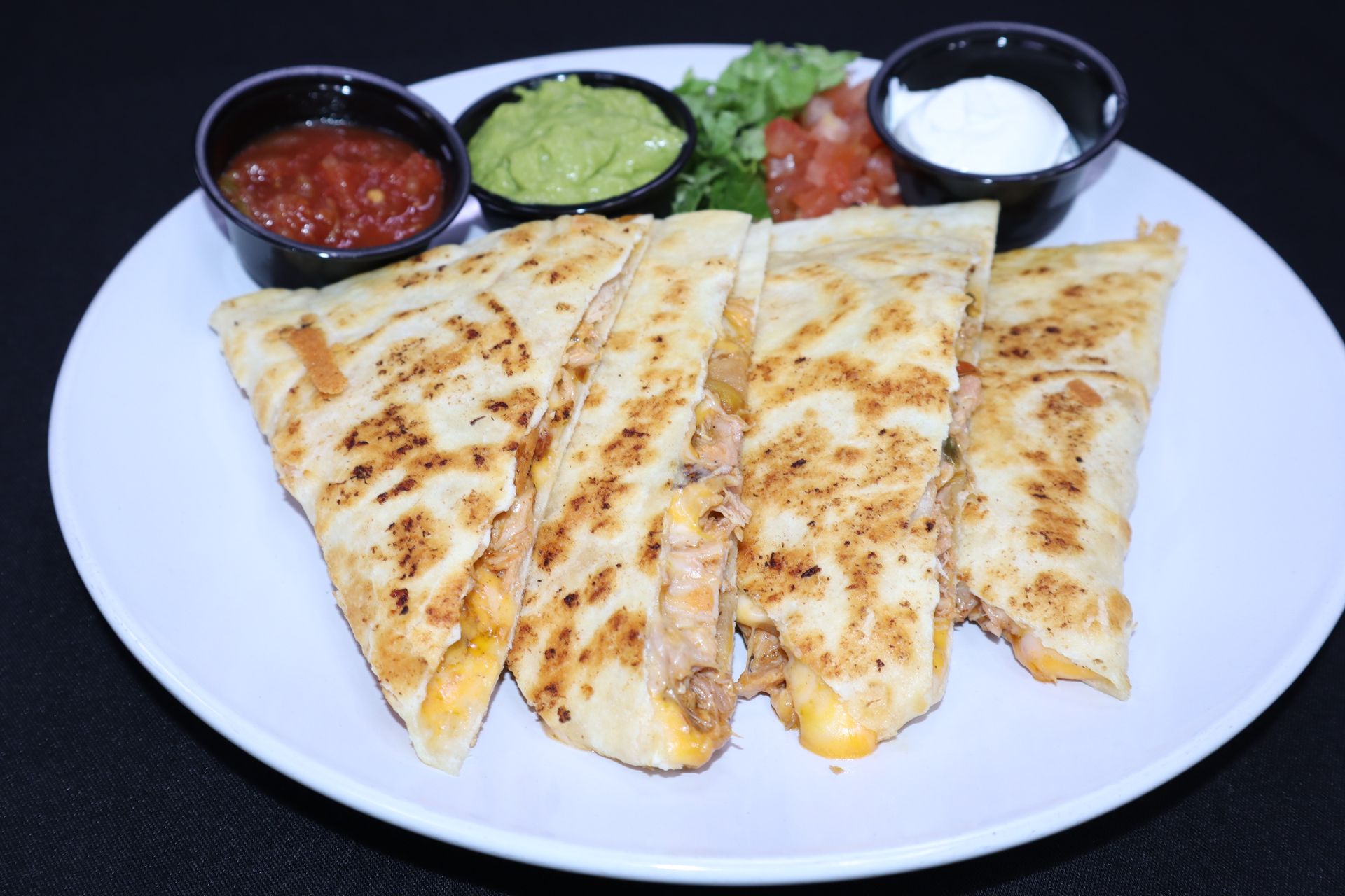 Quesadilla slices with salsa, guacamole, and sour cream on a white plate.