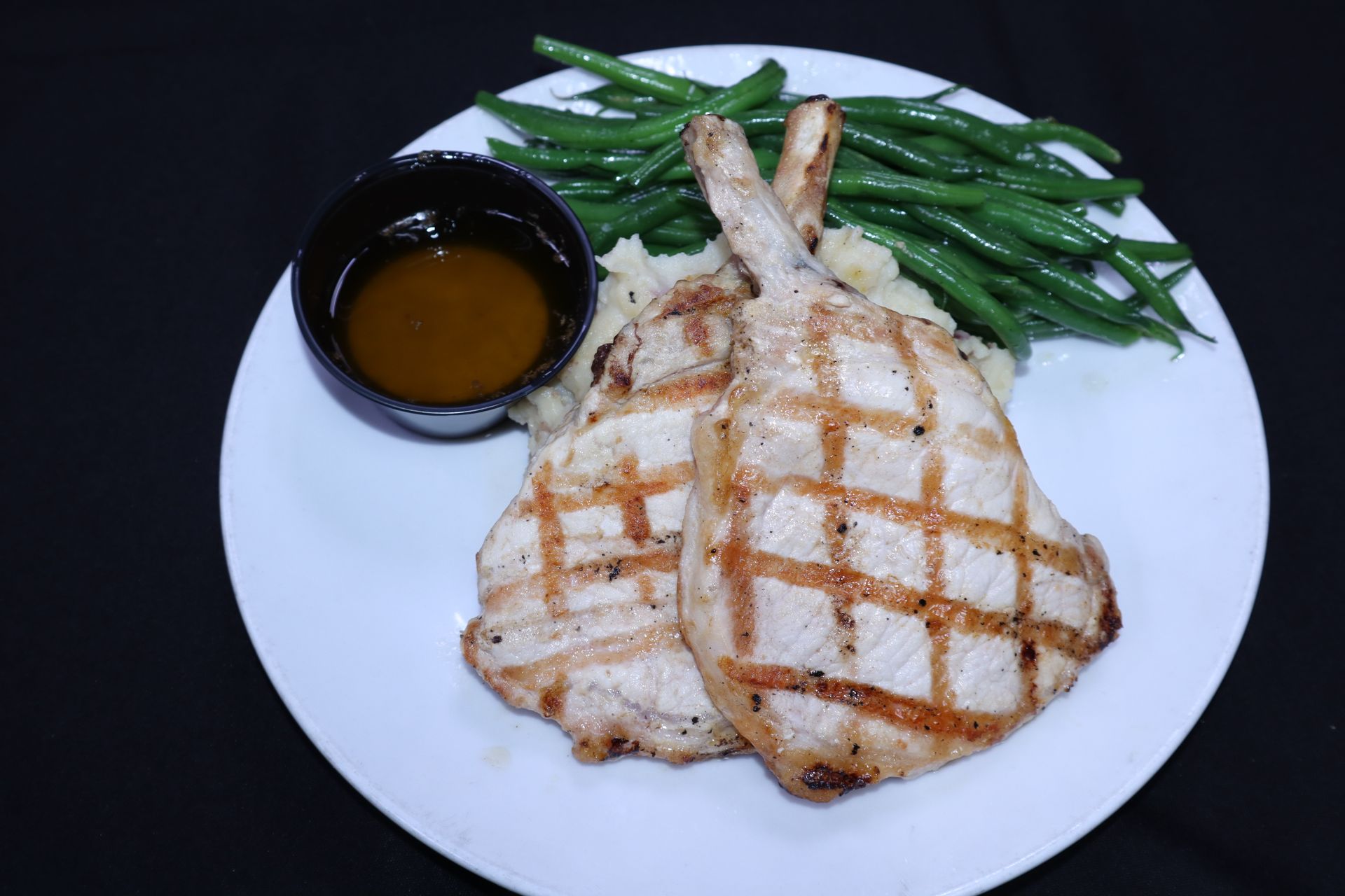Grilled pork chops, mashed potatoes, green beans, and sauce on a white plate.