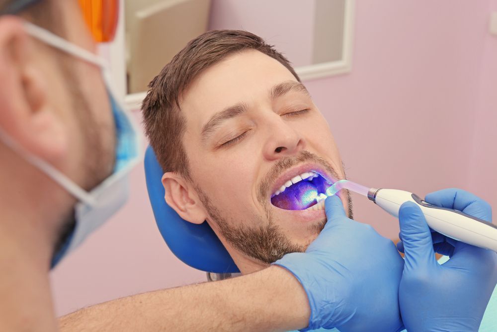 Dentist using a blue light curing tool on a patient's tooth in a dental office. Patient's eyes are closed — Trinity Beach Dental In Trinity Beach, QLD
