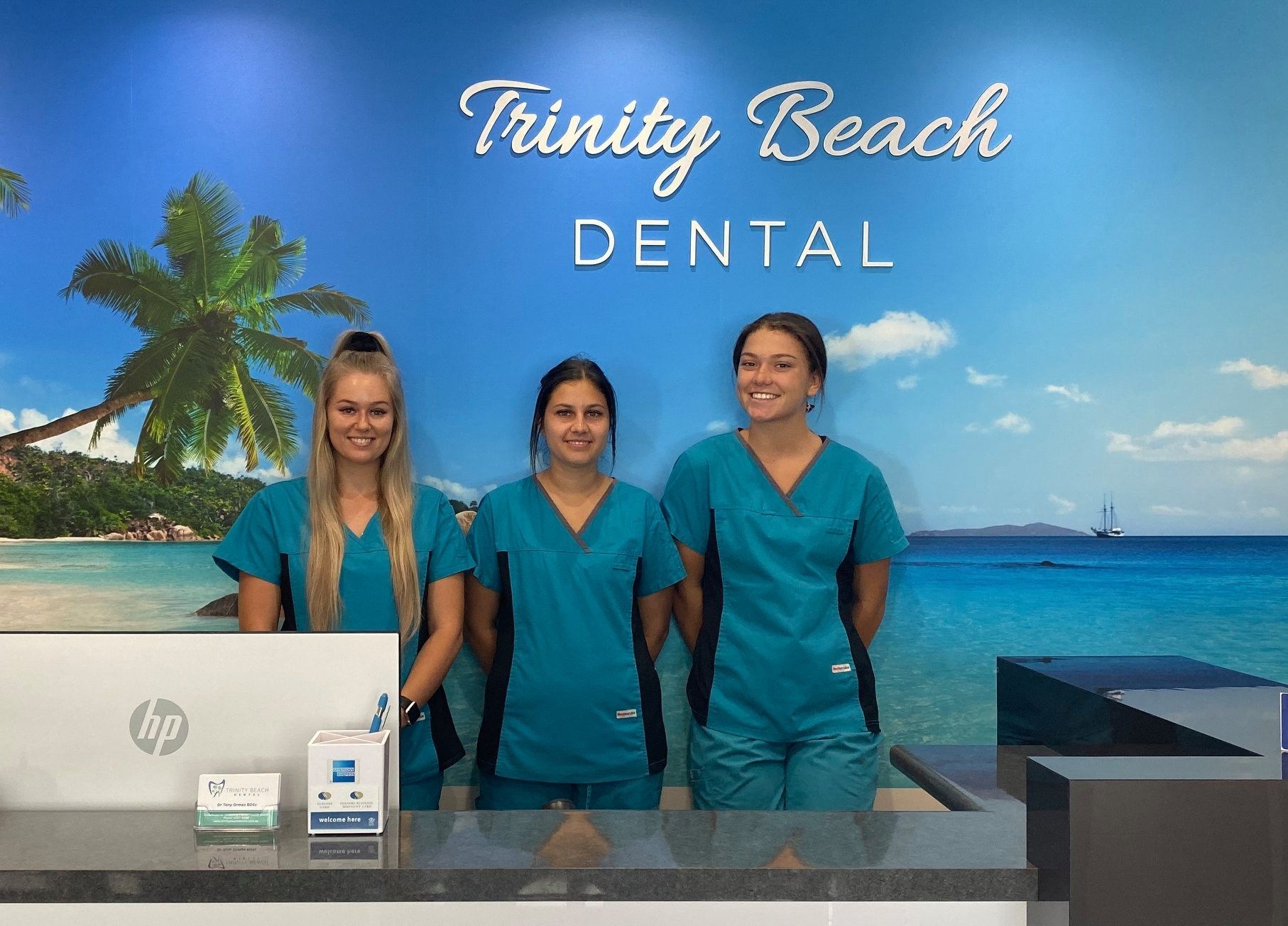 Three Dental Staff in Teal Scrubs Stand Behind a Reception Desk — Trinity Beach Dental In Trinity Beach, QLD