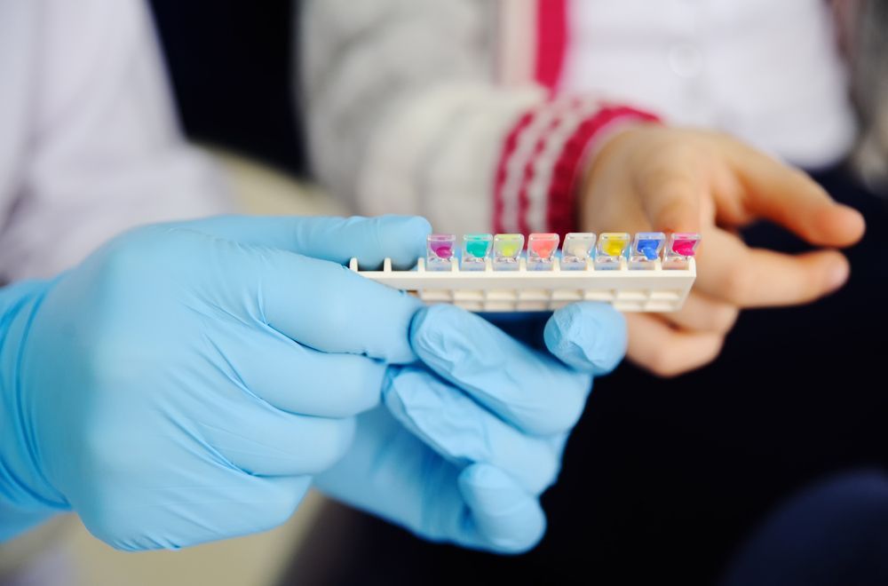 Person in Blue Gloves Holds a Rack of Small Tubes With Colorful Tops — Trinity Beach Dental In Trinity Beach, QLD