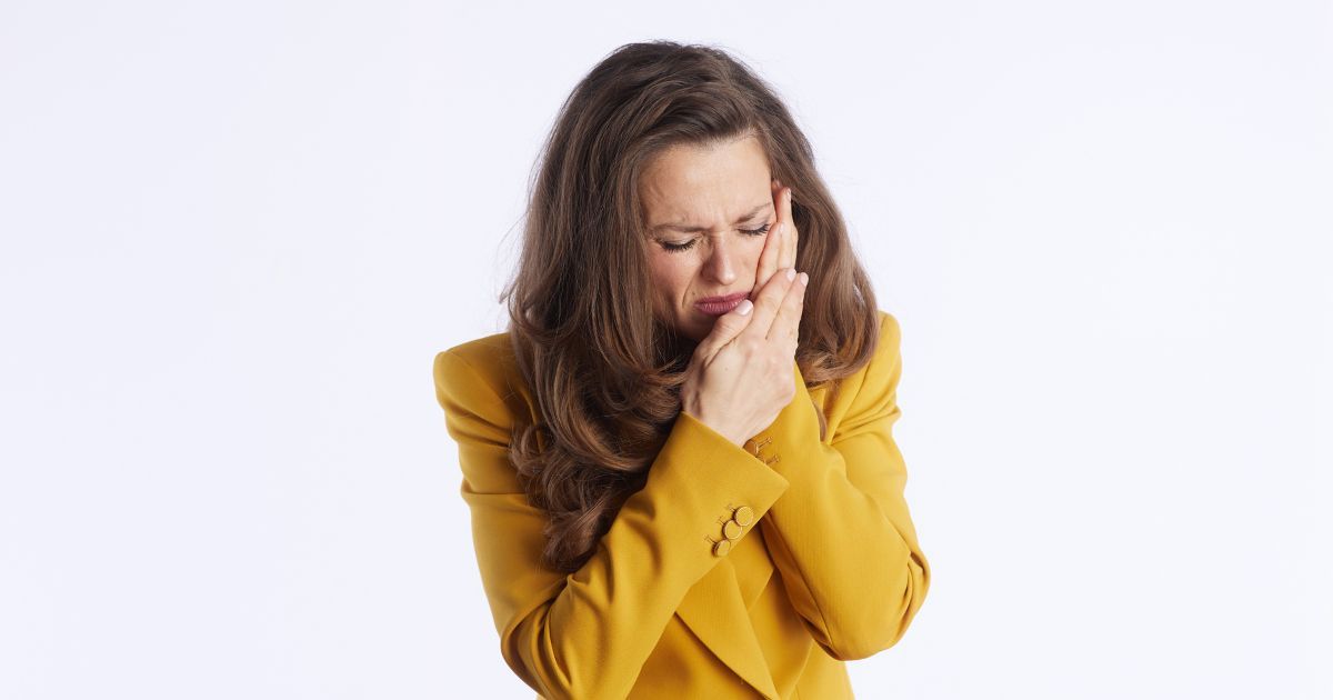 Woman in a Yellow Sweater Covering Her Mouth and Nose — Trinity Beach Dental In Trinity Beach, QLD