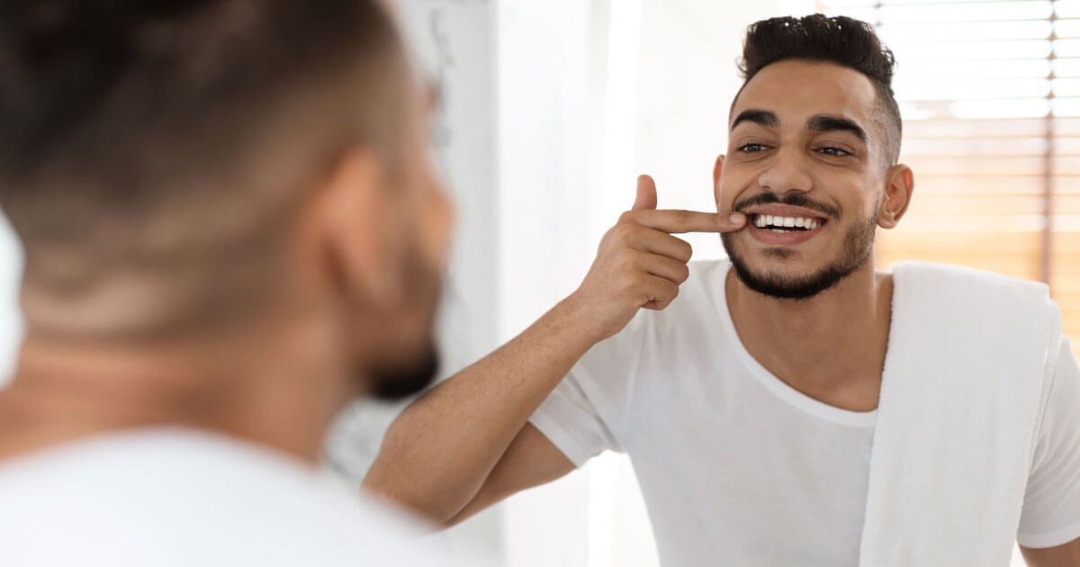 Man Smiling at His Reflection in a Bathroom Mirror — Trinity Beach Dental In Trinity Beach, QLD